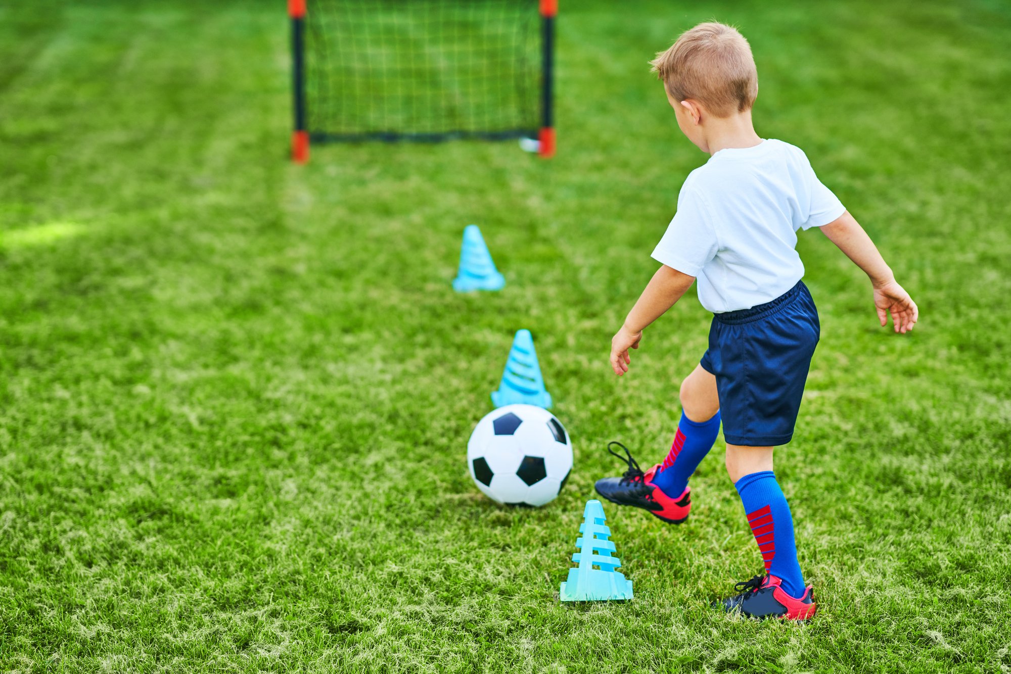 A young boy dribbling a football between training cones